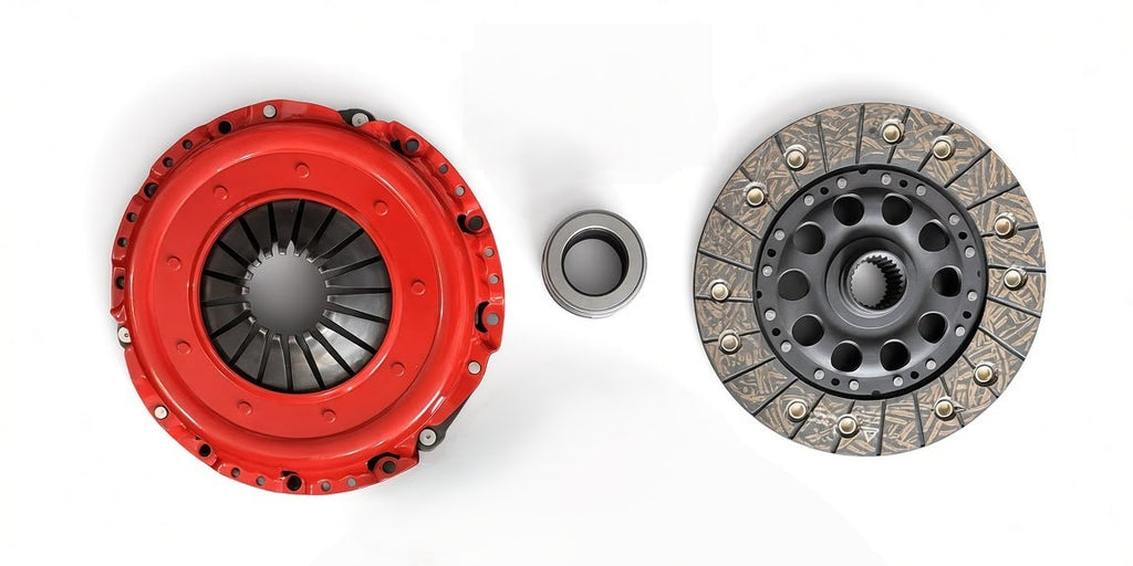 A clutch assembly set featuring a bright red pressure plate, a silver steel journal bearing, and a textured gray clutch disc with gold-toned rivets, arranged on a clean white background.